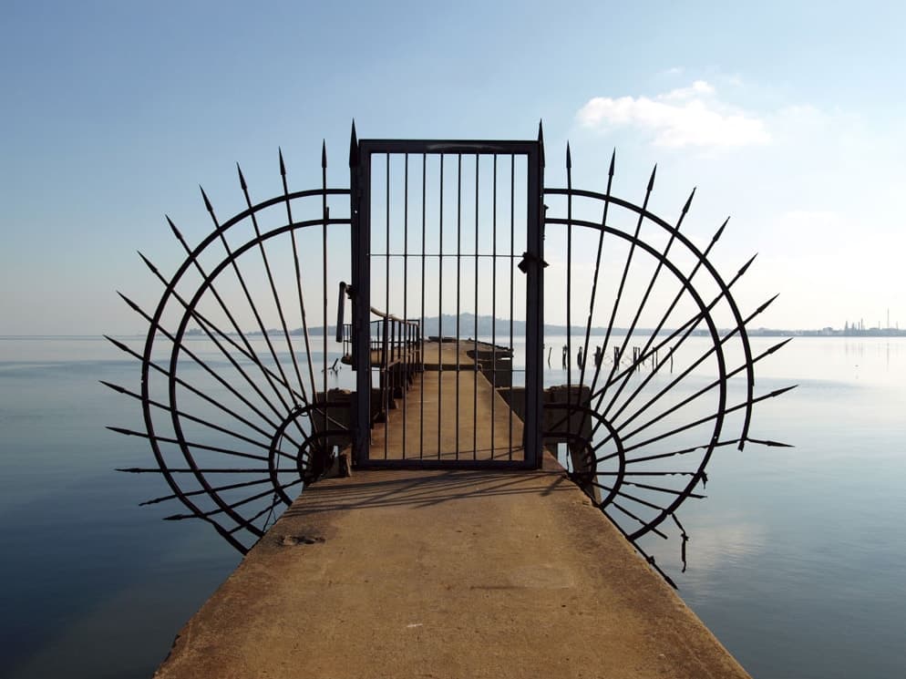 A spiked iron gate standing at the end of a pier over calm water